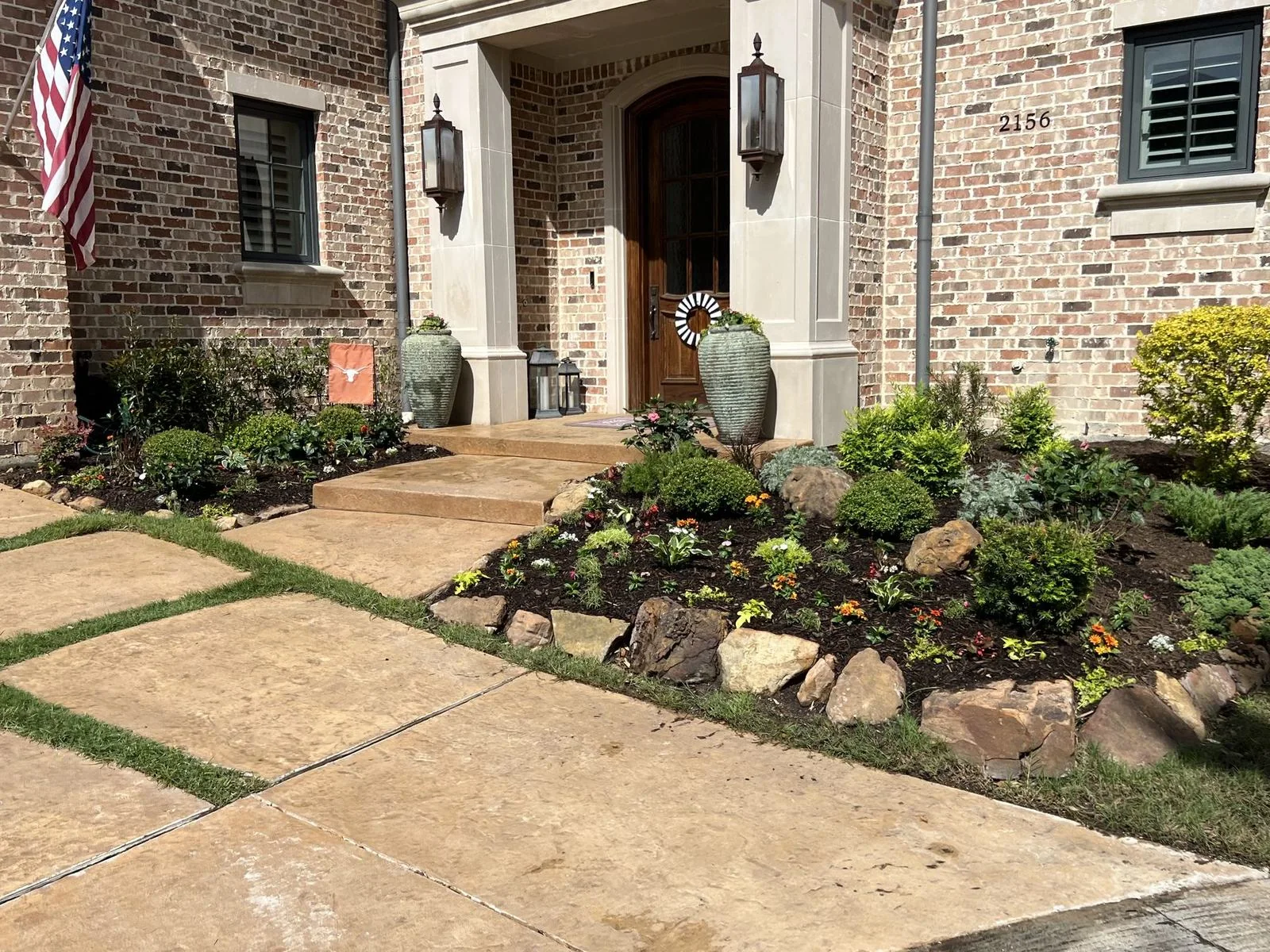 Front yard landscaping by Frisco Landscapes in Plano, TX with a walkway, shrubs, flowers, and stone edging